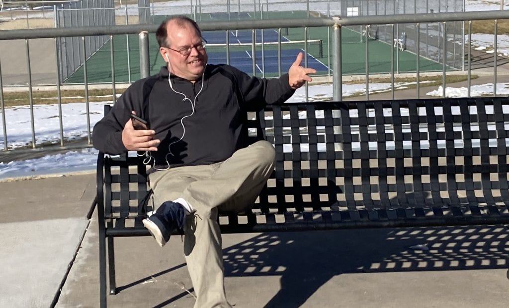 Produce My Book founder, Marty Dickinson, sitting on a park bench writing his Lions Always Win book without typing a word of the manuscript.