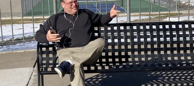 Produce My Book founder, Marty Dickinson, sitting on a park bench writing his Lions Always Win book without typing a word of the manuscript.